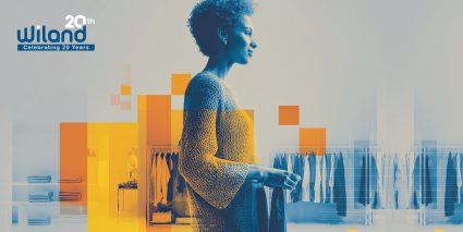 A person stands contemplatively in a modern clothing store, surrounded by neatly organized garments and vibrant geometric shapes.