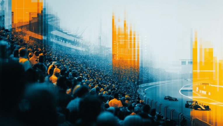 Crowded grandstand overlooks racetrack with two racing cars, overlaid with blue and orange pixelated digital effects.