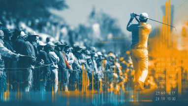 A golfer completing a swing with a crowd standing and watching nearby.