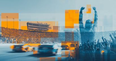 A fan stands and cheers as race cars pass by on the track.
